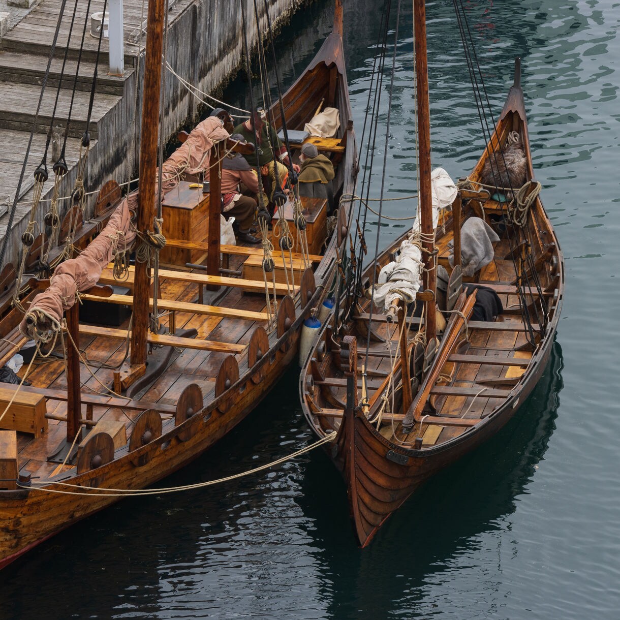 Two traditional wooden Viking ships with tall masts and shields line the harbor pier in Haugesund, Norway, their decks detailed with ropes and sails.