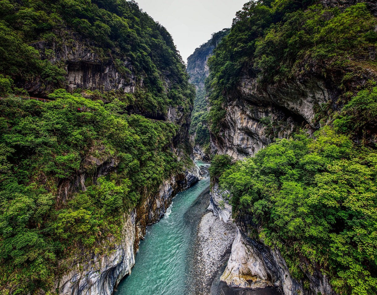 View of Taroko Gorge in Hualien, Taiwan, with steep marble cliffs covered in lush greenery and a turquoise river flowing through the canyon.