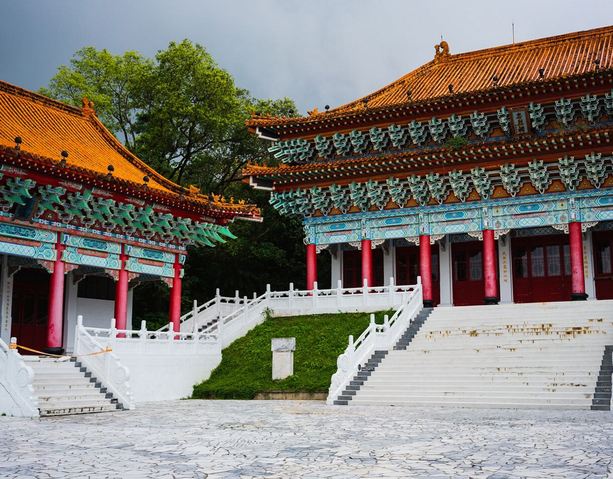 Ornate temple buildings in Hualien, Taiwan, featuring red pillars, colorful carved eaves, and orange tiled roofs surrounded by lush greenery.