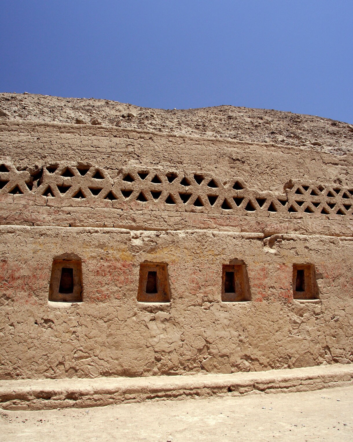 Close view of an adobe wall at Tambo Colorado featuring trapezoid windows and geometric ventilation openings.