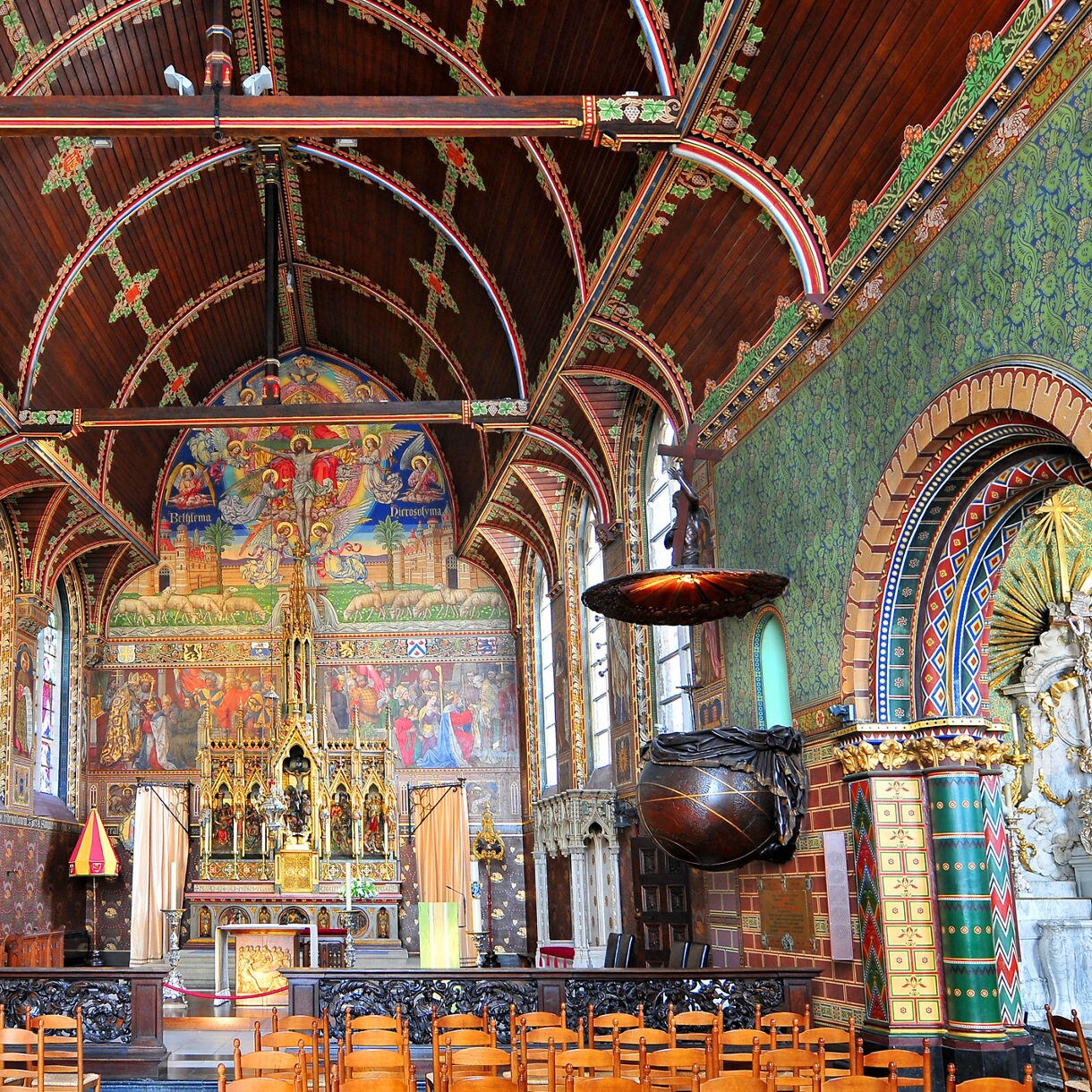  Interior of the Basilica of the Holy Blood in Bruges, Belgium, with vibrant stained glass, ornate painted walls, arched wooden ceiling and a richly decorated altar.