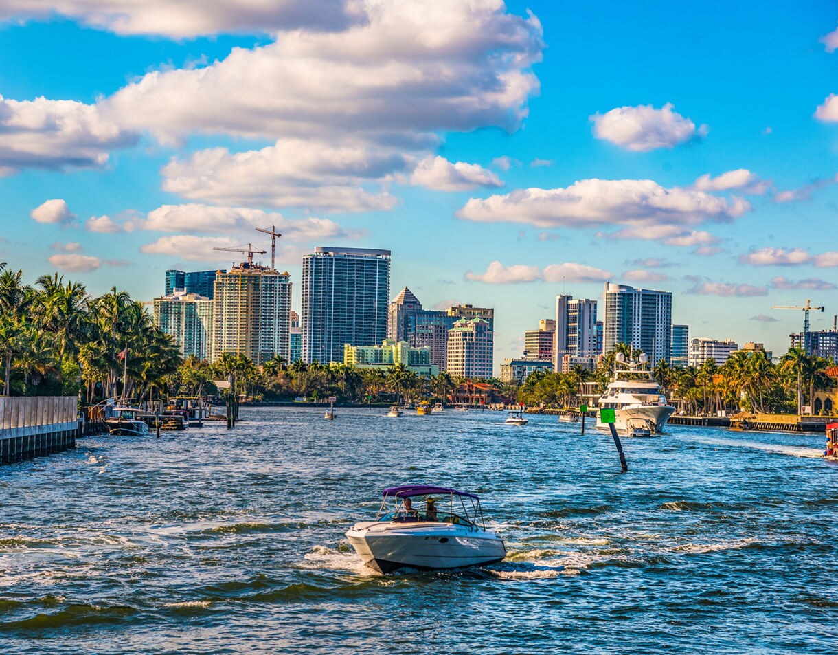 Boats navigating the Intracoastal Waterway with palm-lined shores and Miami’s modern high-rise buildings in the background beneath a bright sky with scattered clouds.