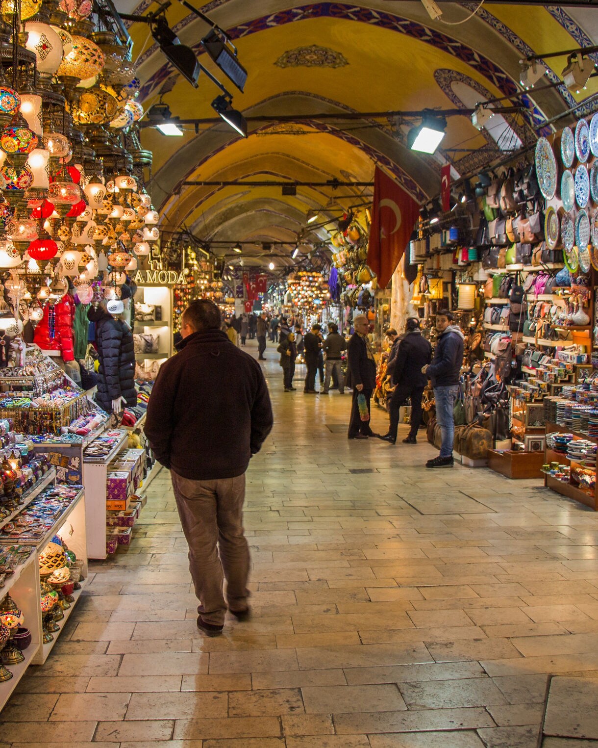 Interior of Istanbul’s Grand Bazaar lined with stalls selling colorful mosaic lamps, decorative plates and traditional crafts under arched ceilings.