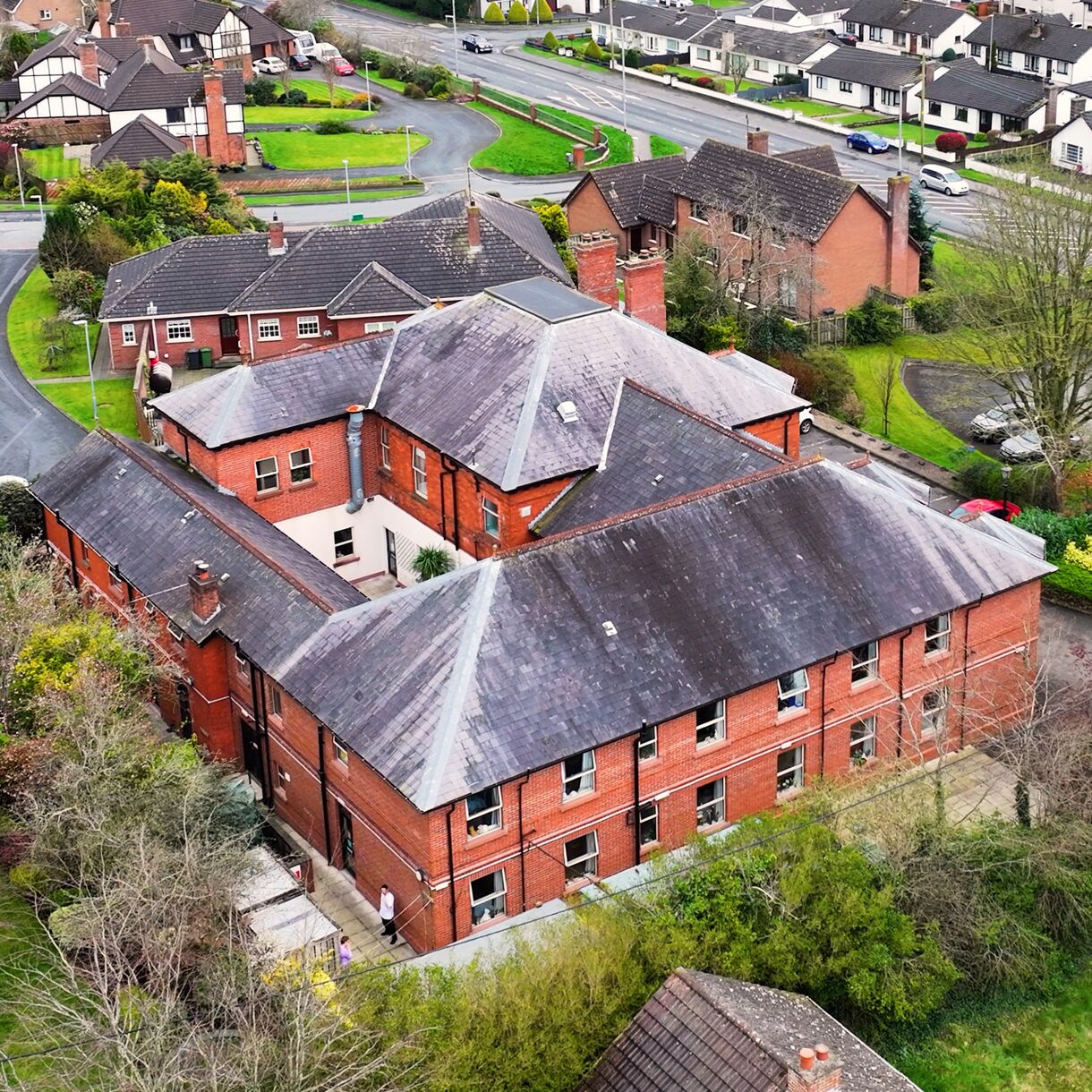 Aerial view of Iveagh House in Banbridge, showing a large red-brick building with a slate roof surrounded by suburban homes and greenery.