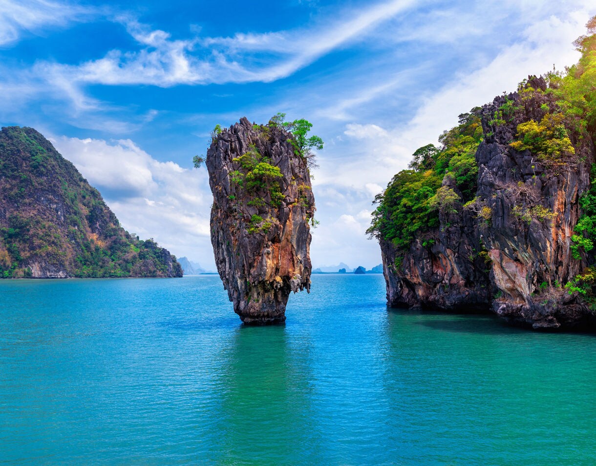 Towering limestone karst standing alone in the turquoise sea at James Bond Island, framed by lush cliffs and blue sky.