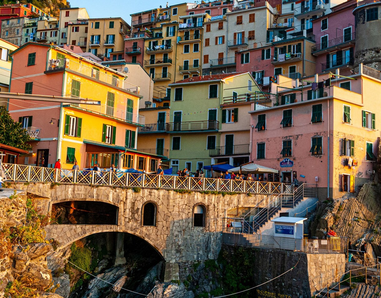 Colorful cliffside houses in Cinque Terre glowing in warm evening light with a stone bridge and seaside terraces below.