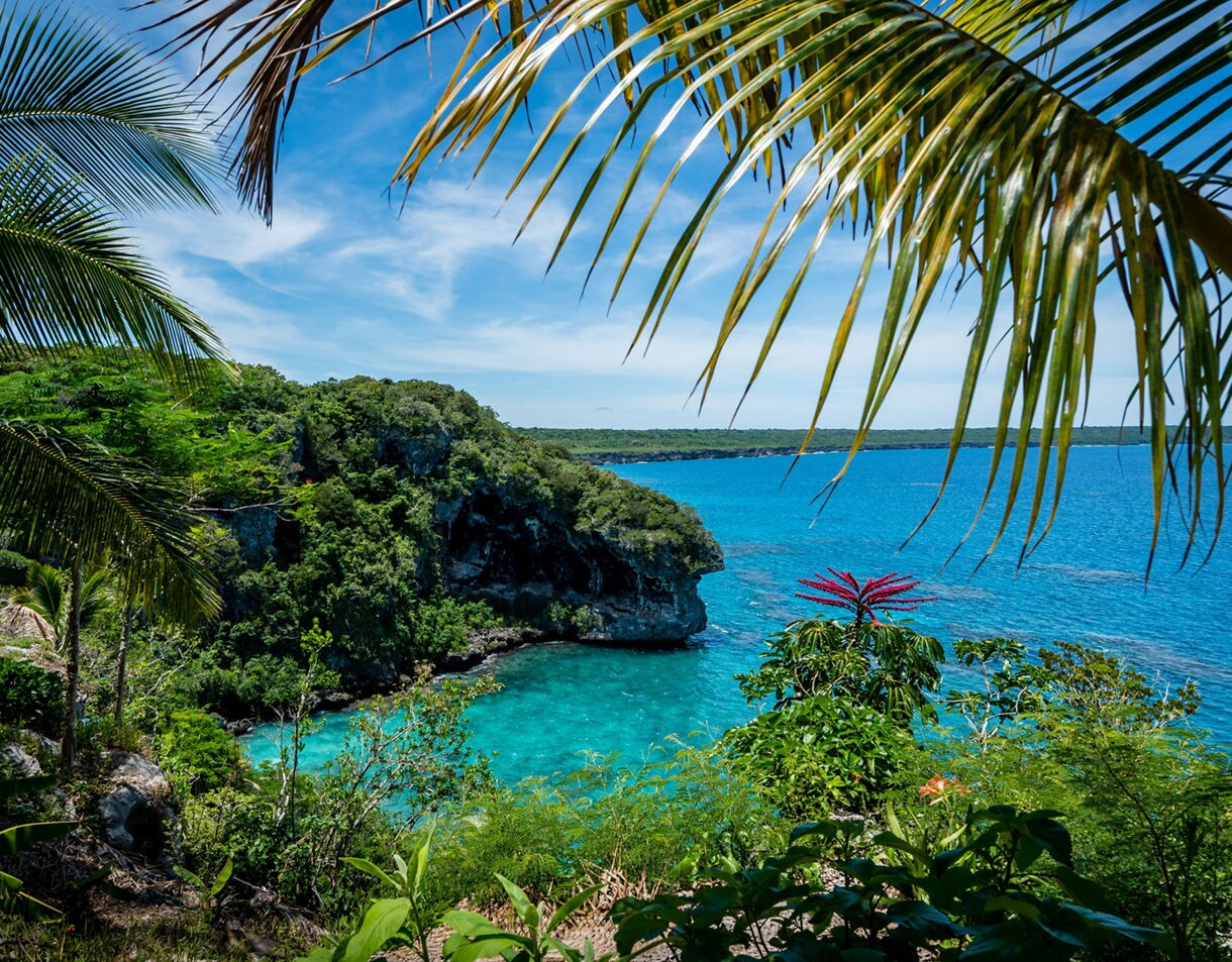 View of lush green foliage framing the steep limestone cliffs of Jokin above vibrant turquoise water in Lifou, New Caledonia.