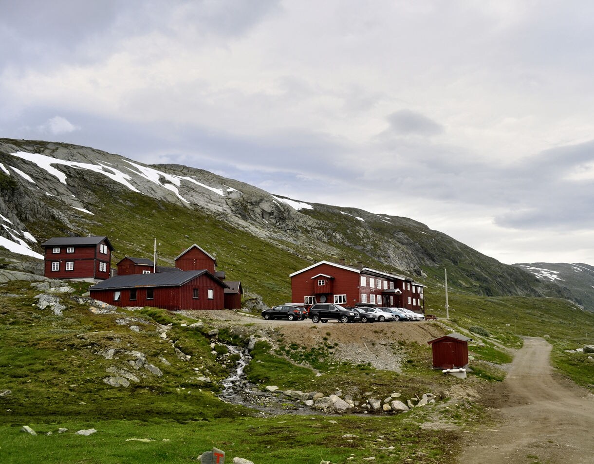 Cluster of red mountain lodges in Jotunheimen National Park, Norway, set against rocky hillsides with patches of snow under an overcast sky.