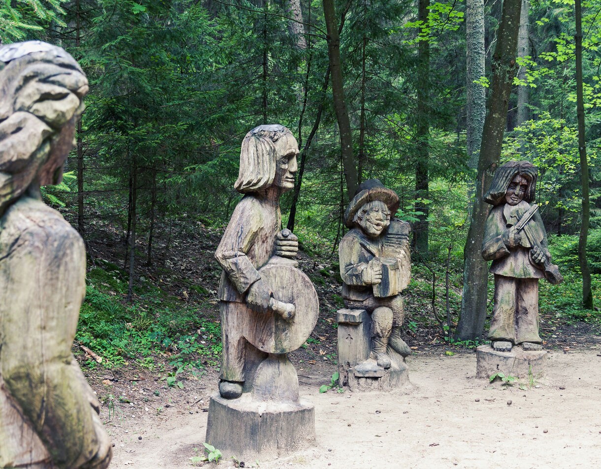Carved wooden sculptures of musicians in a forest clearing at Juodkrantė, Lithuania, surrounded by trees and greenery.