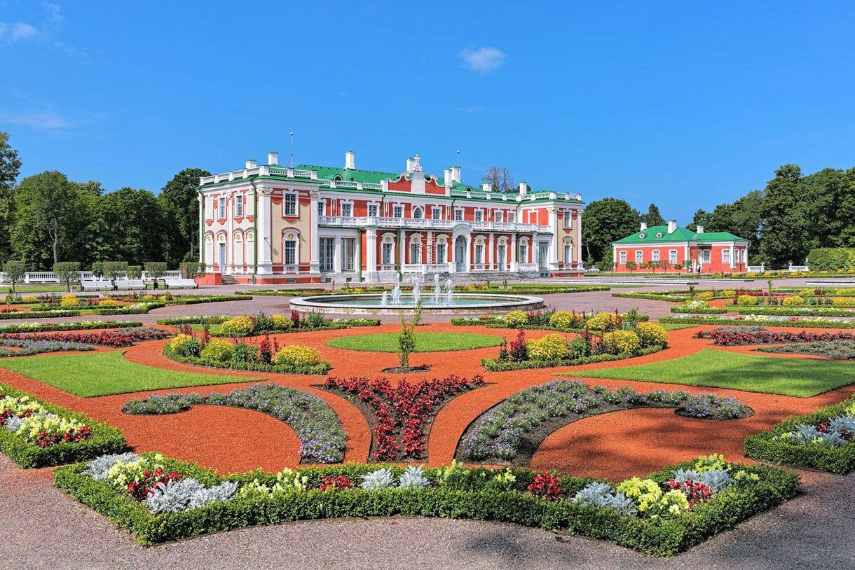 Kadriorg Palace in Tallinn, Estonia, a red-and-white baroque building with green roofs, set behind ornate symmetrical gardens and a central fountain.