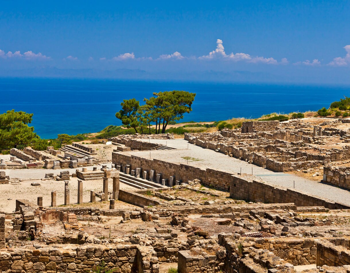 Ruins of the ancient city of Kamiros on Rhodes, Greece, overlooking the bright blue Aegean Sea under a clear summer sky.