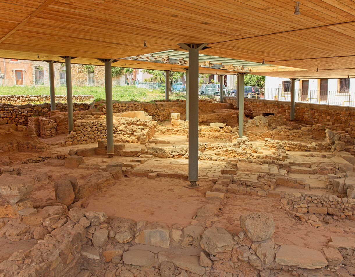 Excavated ruins at Kastelli Hill in Chania, Crete, showing ancient stone foundations and walls protected under a wooden roofed structure.
