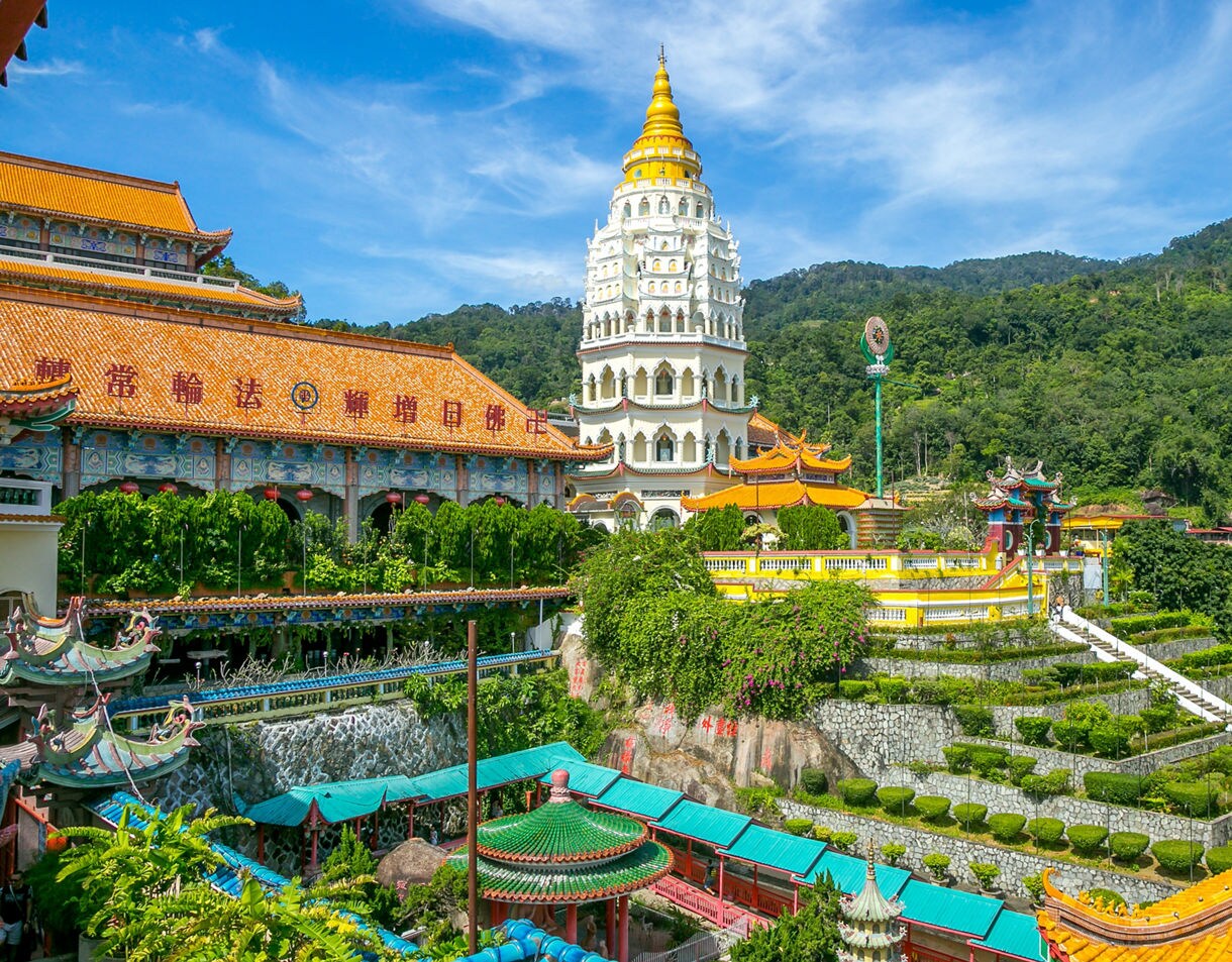 Kek Lok Si Temple in Penang with its striking white and gold pagoda, orange-roofed halls and terraced gardens against green hills.