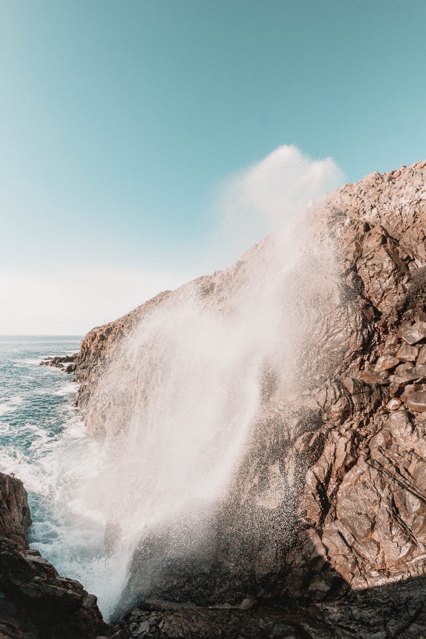 Seawater shooting high into the air from rocky cliffs at La Bufadora blowhole under a clear blue sky.