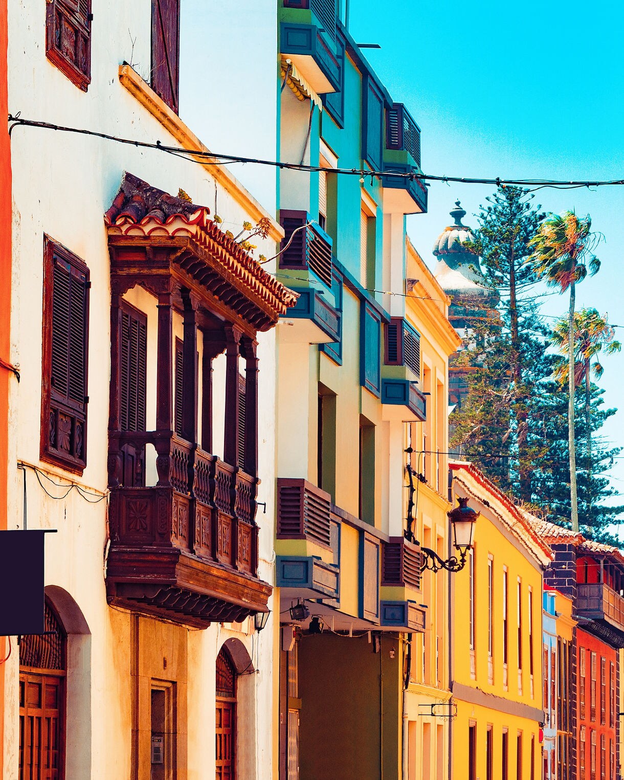Colorful colonial-style buildings with wooden balconies and shutters lining a sunny street in San Cristóbal de La Laguna, Tenerife.