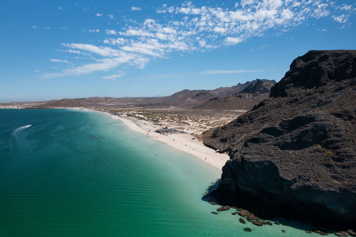 Aerial view of La Paz, Mexico with emerald-green sea, wide sandy beach and rocky cliffs under a blue sky