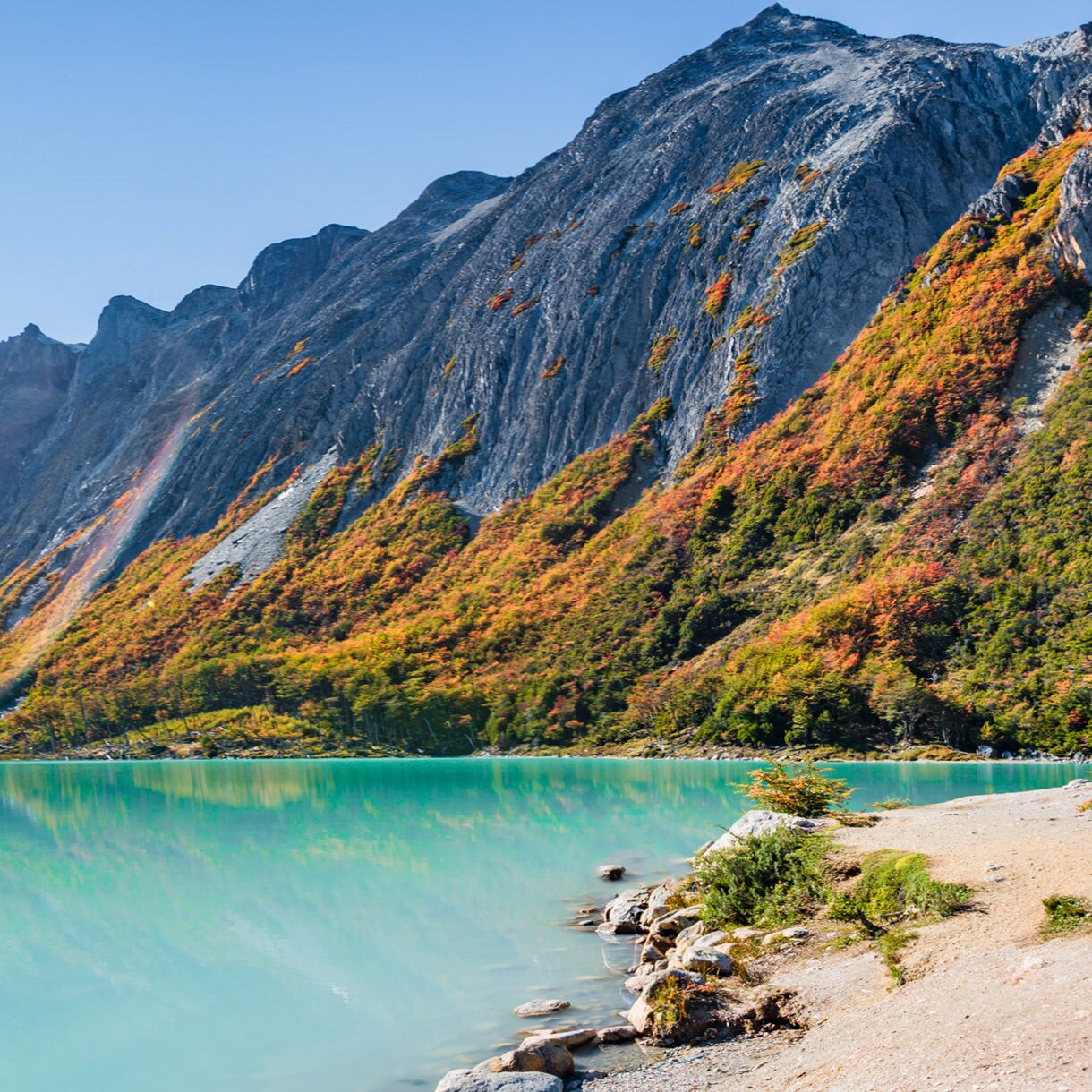 Turquoise Lake Esmeralda surrounded by steep rocky mountains and autumn foliage, with bright sunlight reflecting off the calm water.