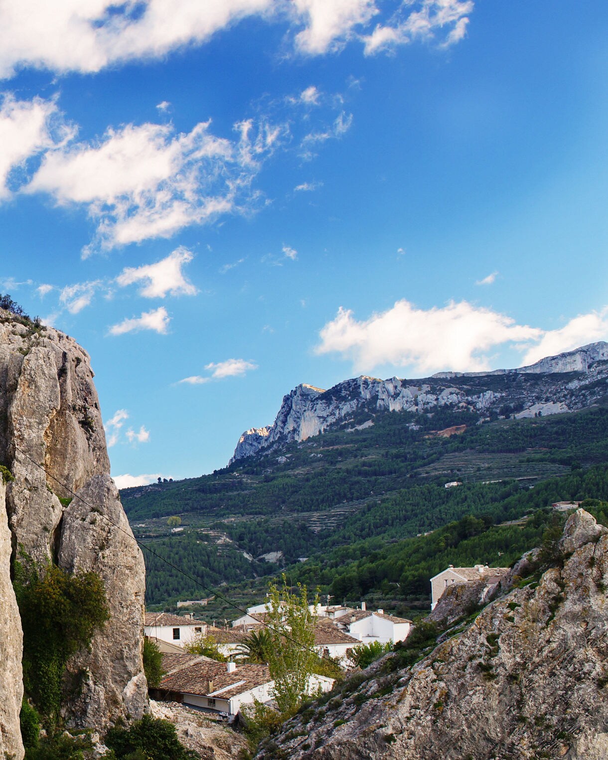 Ancient stone fortress ruins built into rocky cliffs with mountains and green valleys in the background.