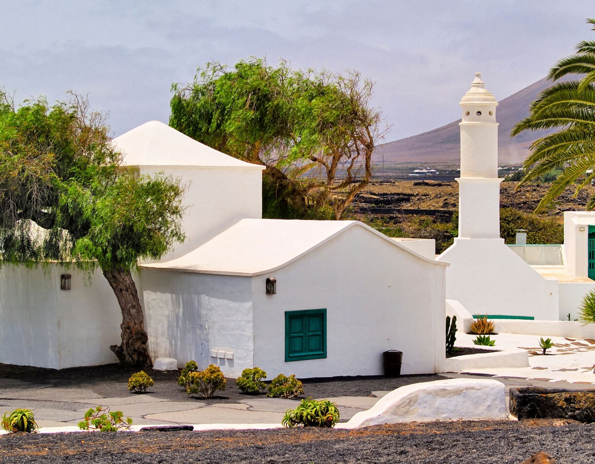 White buildings with green shutters and a tower surrounded by palm trees and lava rock in Lanzarote.