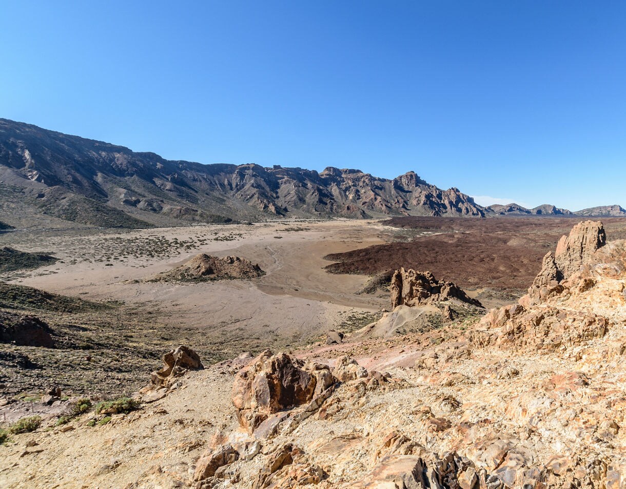 Expansive view of Las Cañadas National Park in Tenerife, featuring rocky volcanic terrain, lava fields and surrounding mountain ridges under a clear blue sky.