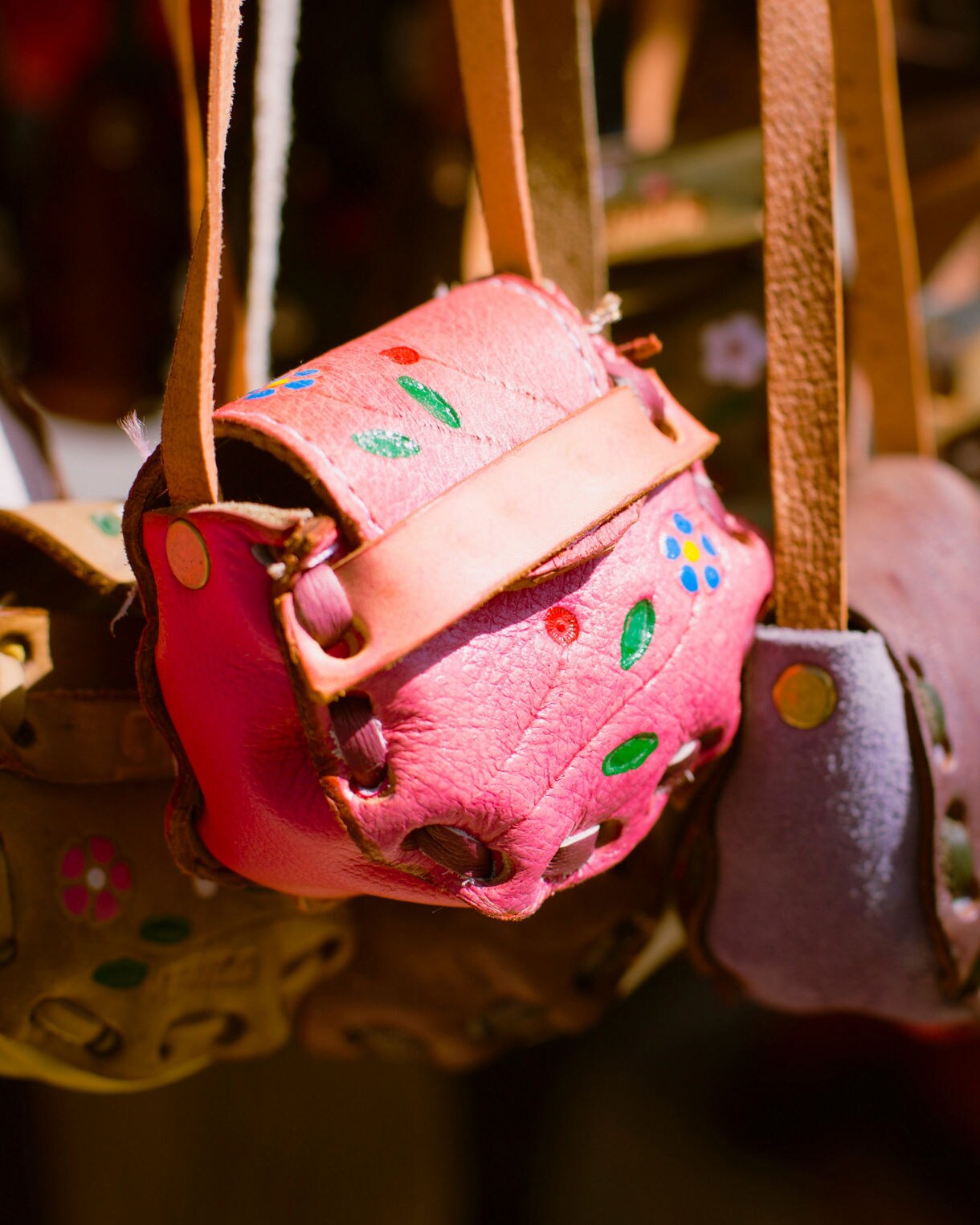 Close-up of small colorful leather purses with floral designs hanging in a market stall.