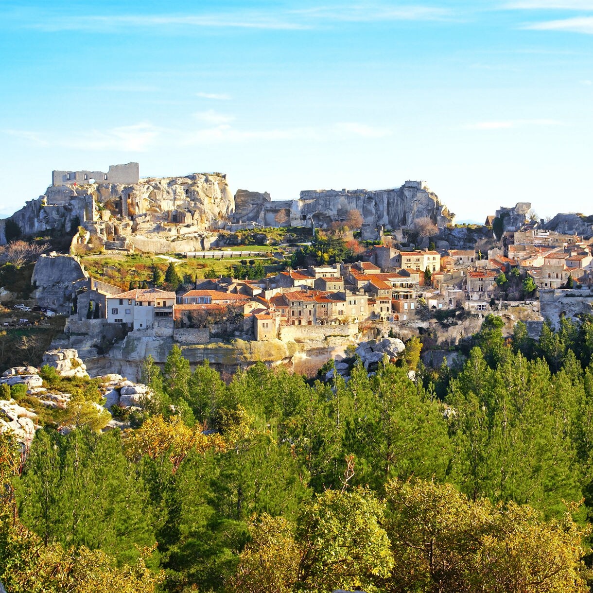 Scenic view of Les Baux-de-Provence, a medieval village with stone houses and fortress ruins perched on rocky cliffs surrounded by green hills.