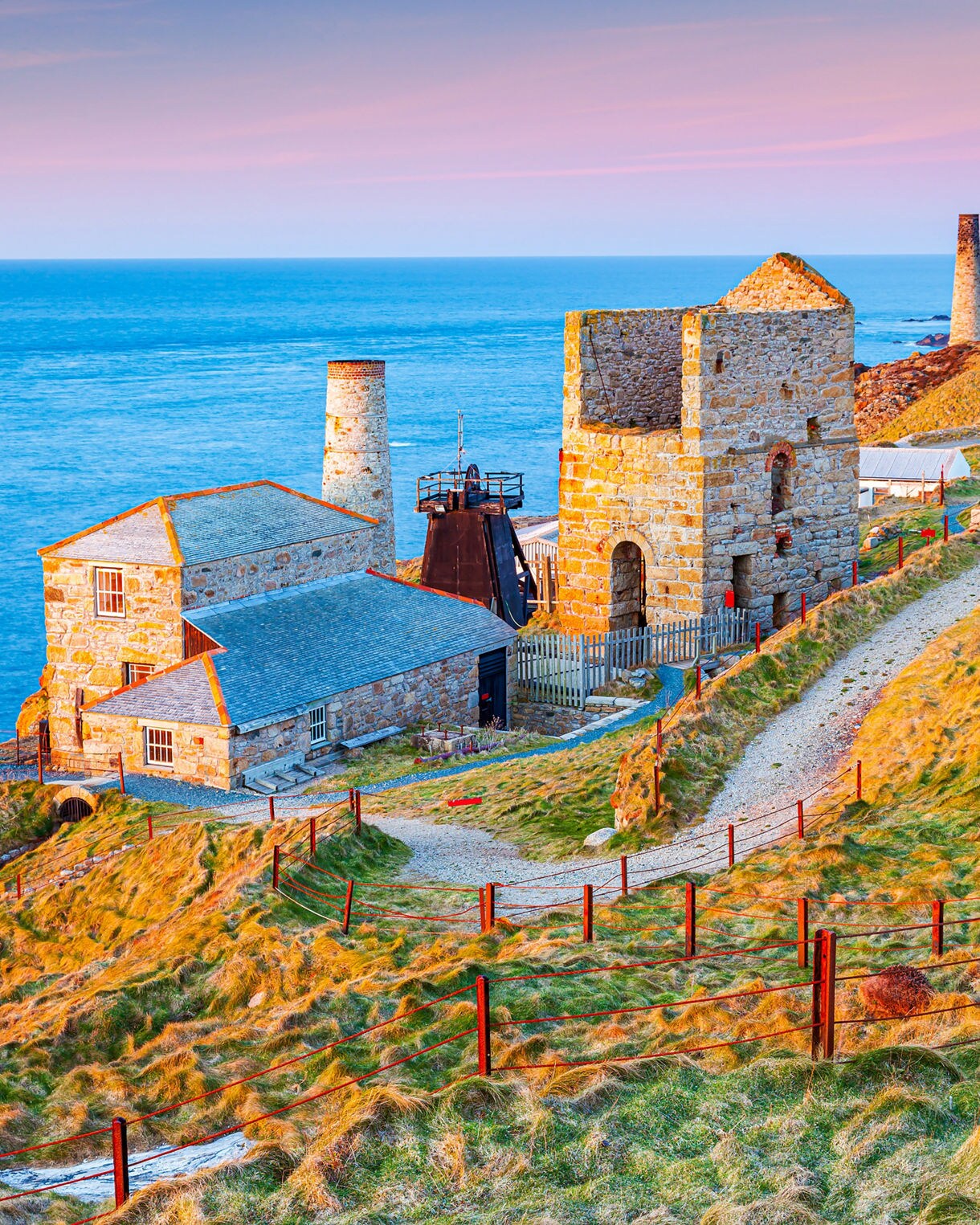 Historic stone buildings and chimneys of Levant Mine on Cornwall’s coastline, set against the blue Atlantic Ocean.