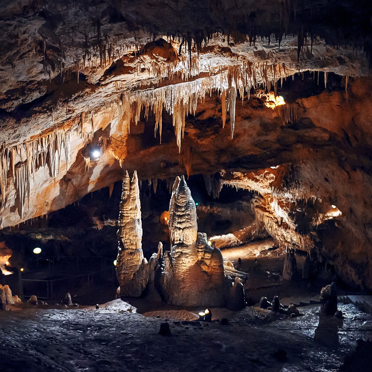 Lipa Cave interior with sharp stalactites hanging from the ceiling and tall stalagmites rising from the cave floor, softly lit to highlight the rock formations.