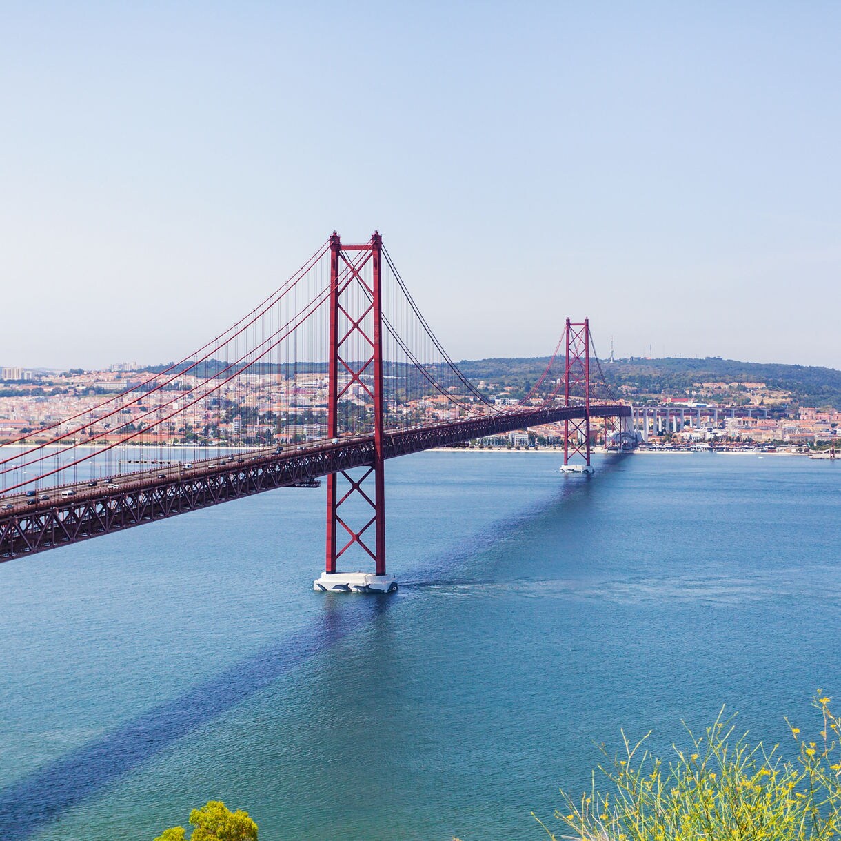Panoramic view of the red suspension 25th of April Bridge spanning the Tagus River in Lisbon, Portugal, with the cityscape in the background.