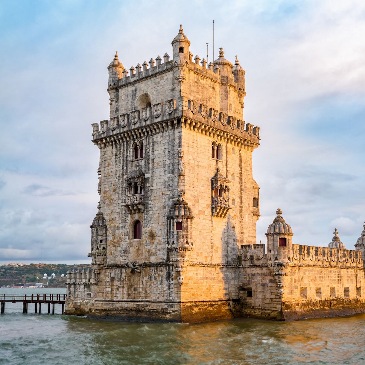 Belém Tower in Lisbon, Portugal, a historic 16th-century fortress with ornate stonework rising from the Tagus River at sunset.