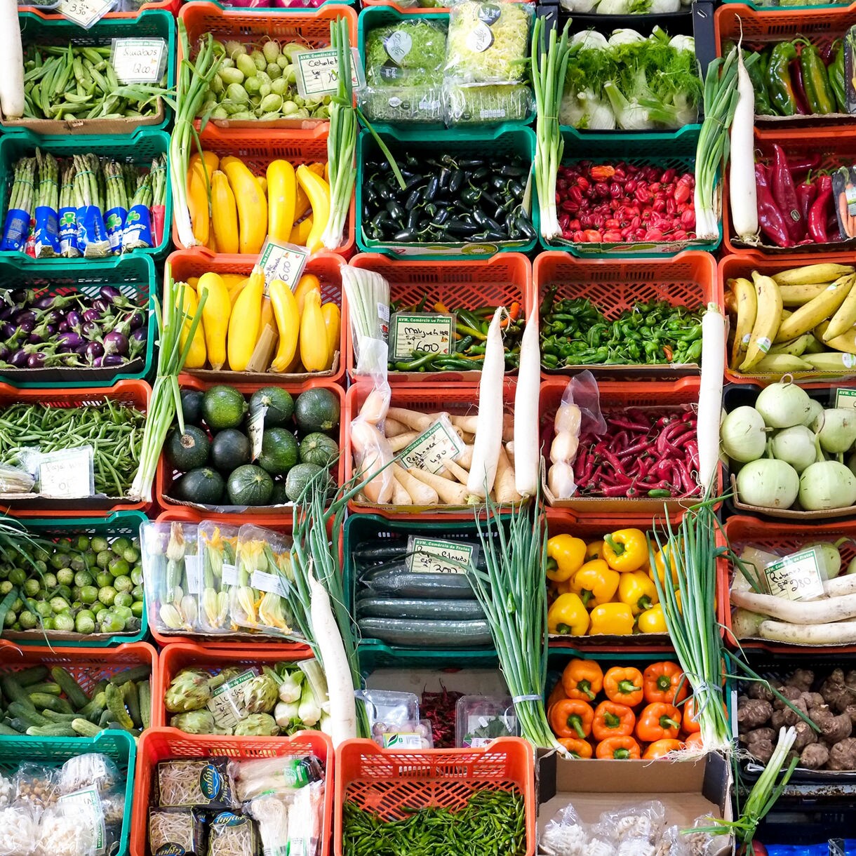 Colorful display of fruits and vegetables arranged in baskets at a Lisbon market, including peppers, squash, avocados, beans and greens.