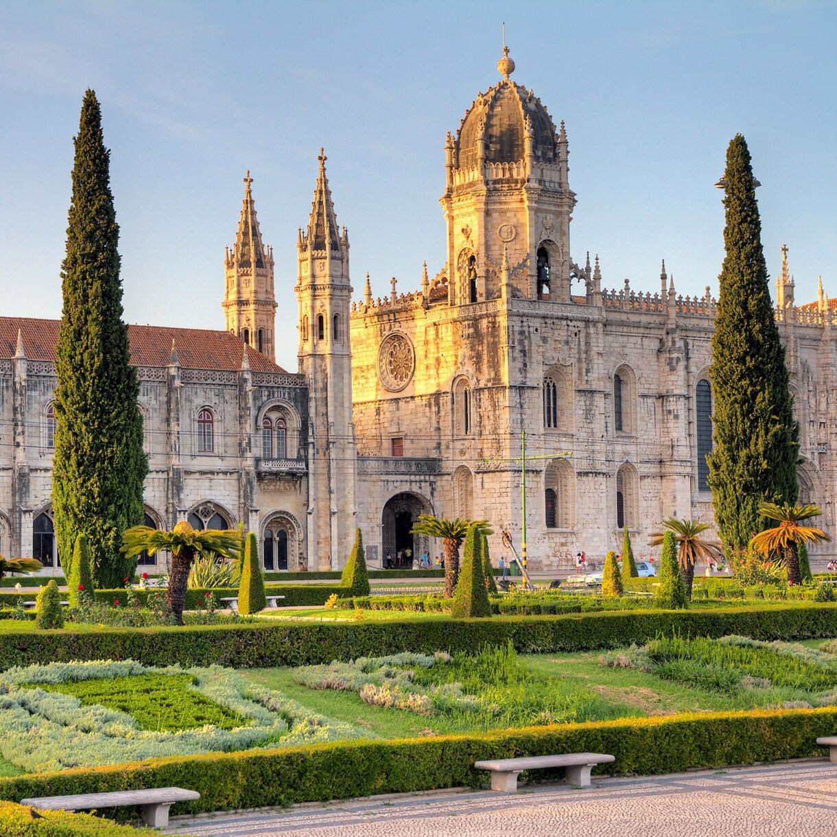 Exterior of Jerónimos Monastery in Lisbon, featuring ornate Gothic details, towers and a manicured garden in the foreground.