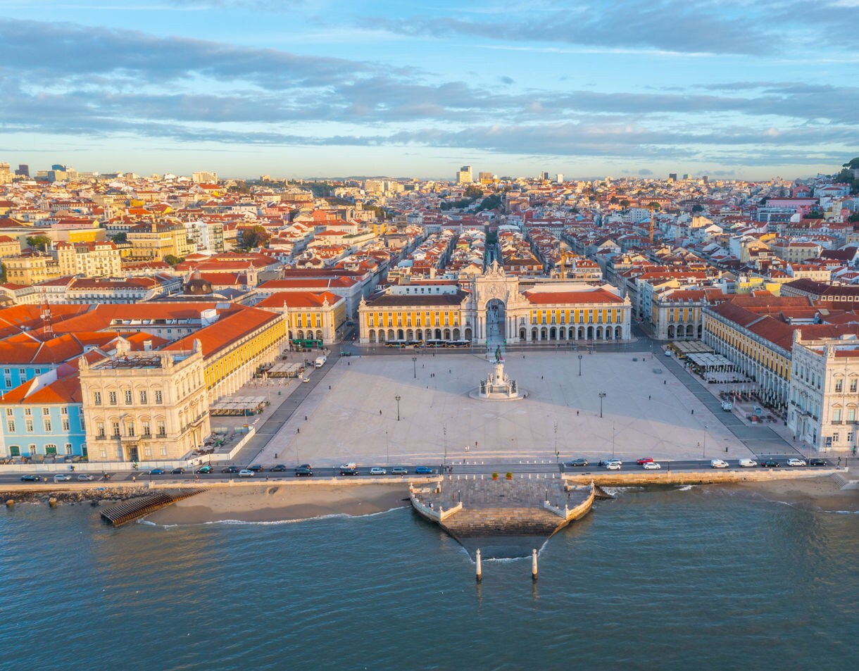 Aerial view of Lisbon’s Praça do Comércio with yellow arcaded buildings, central statue and riverside promenade leading to the Tagus.