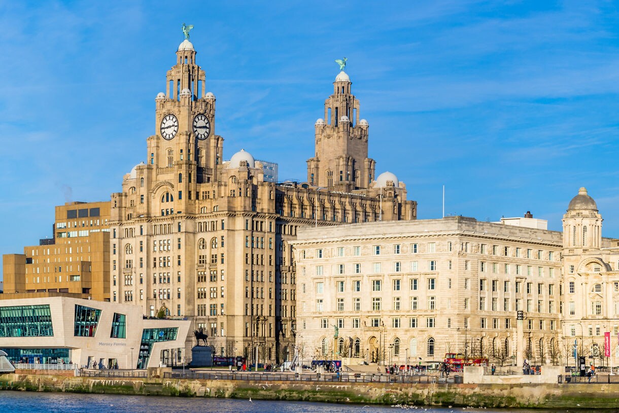 Panoramic view of Liverpool’s waterfront featuring the Royal Liver Building, Port of Liverpool Building and modern structures under a bright blue sky.