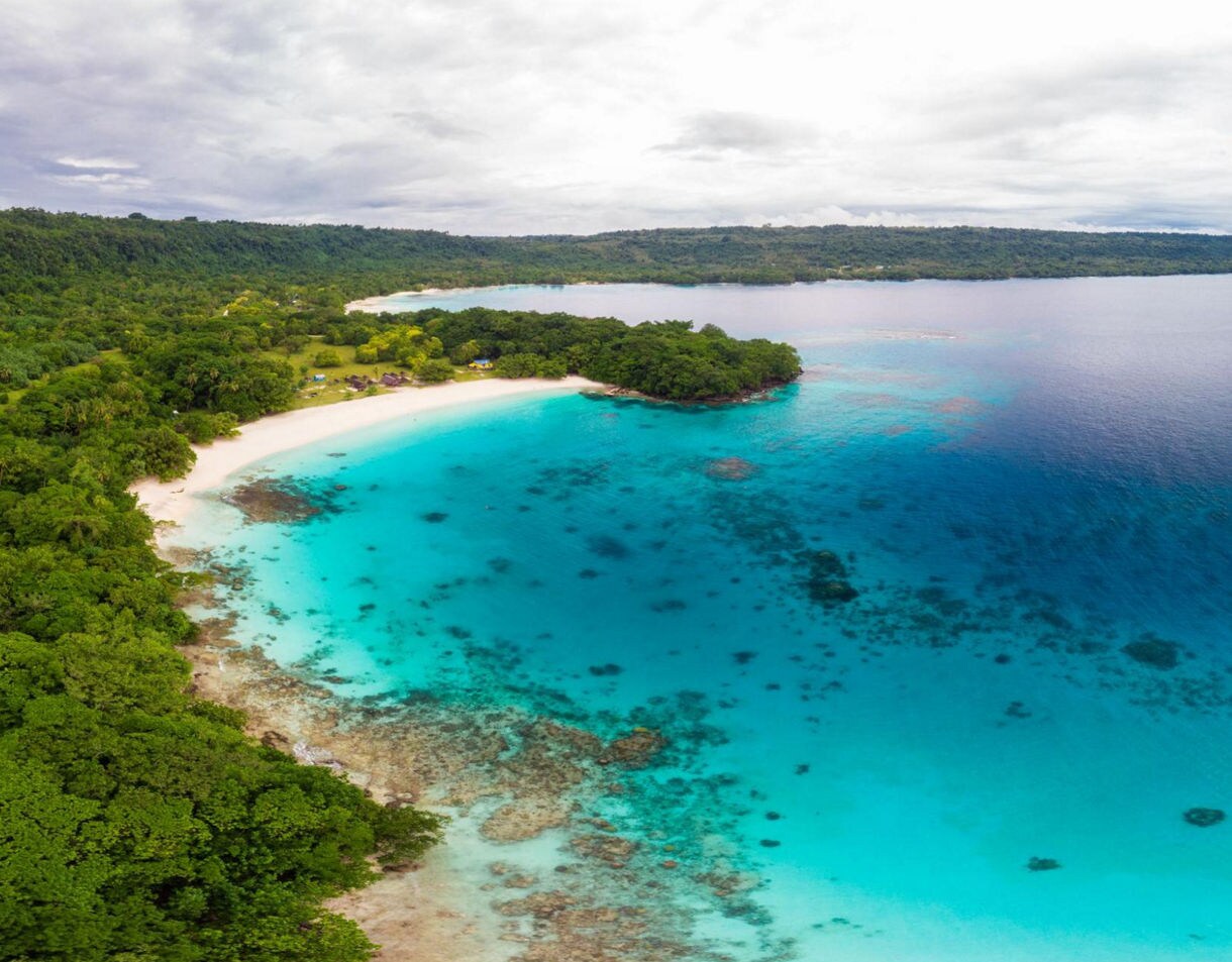 Aerial view of Champagne Beach with bright turquoise water, white sand and dense green tropical forest along the shoreline.