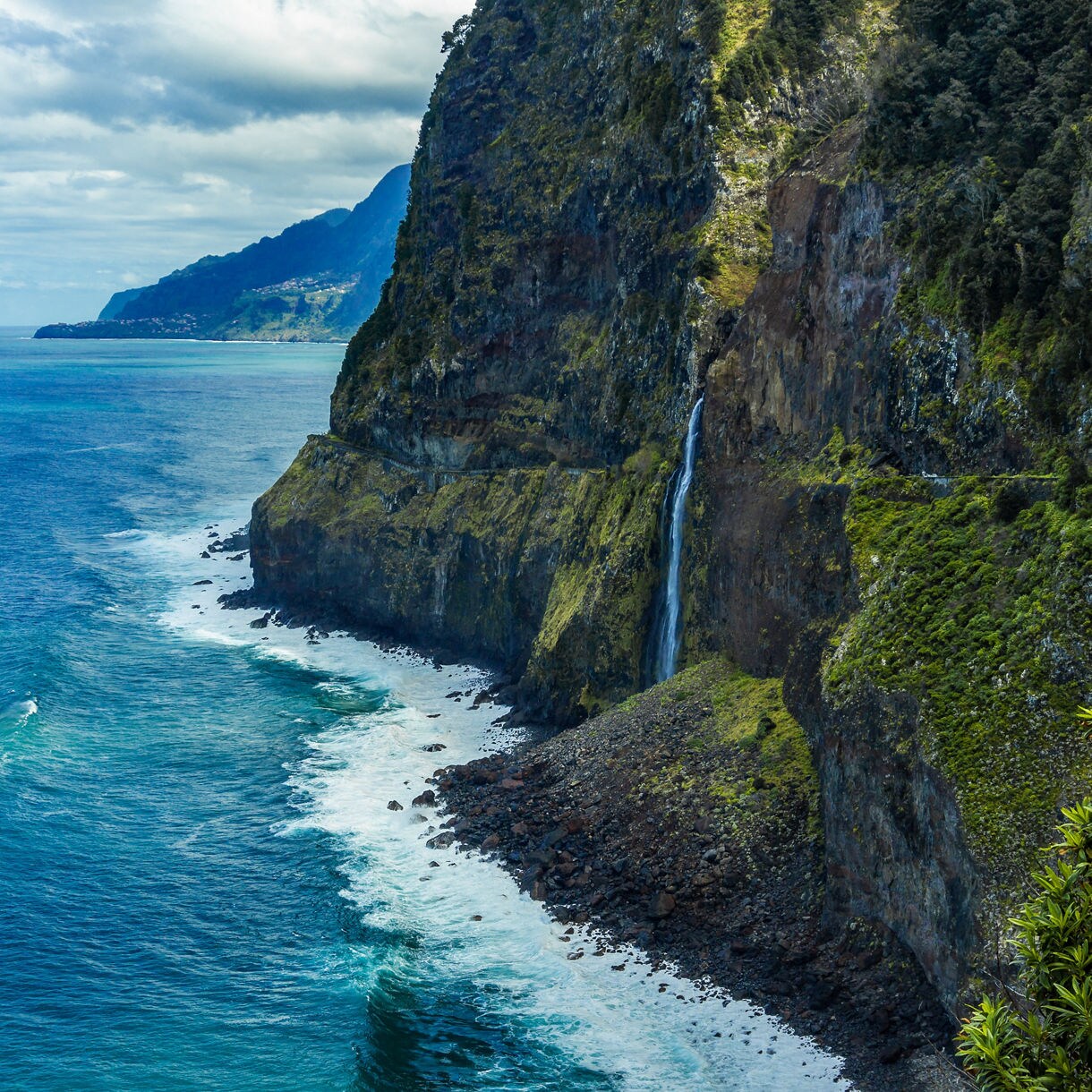 Tall waterfall plunging from lush green cliffs into the ocean along Madeira’s rugged northern coastline.
