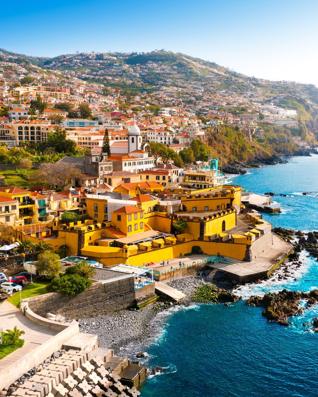 Bright yellow São Tiago Fortress in Funchal, Madeira, perched by the sea with hillside homes rising behind.