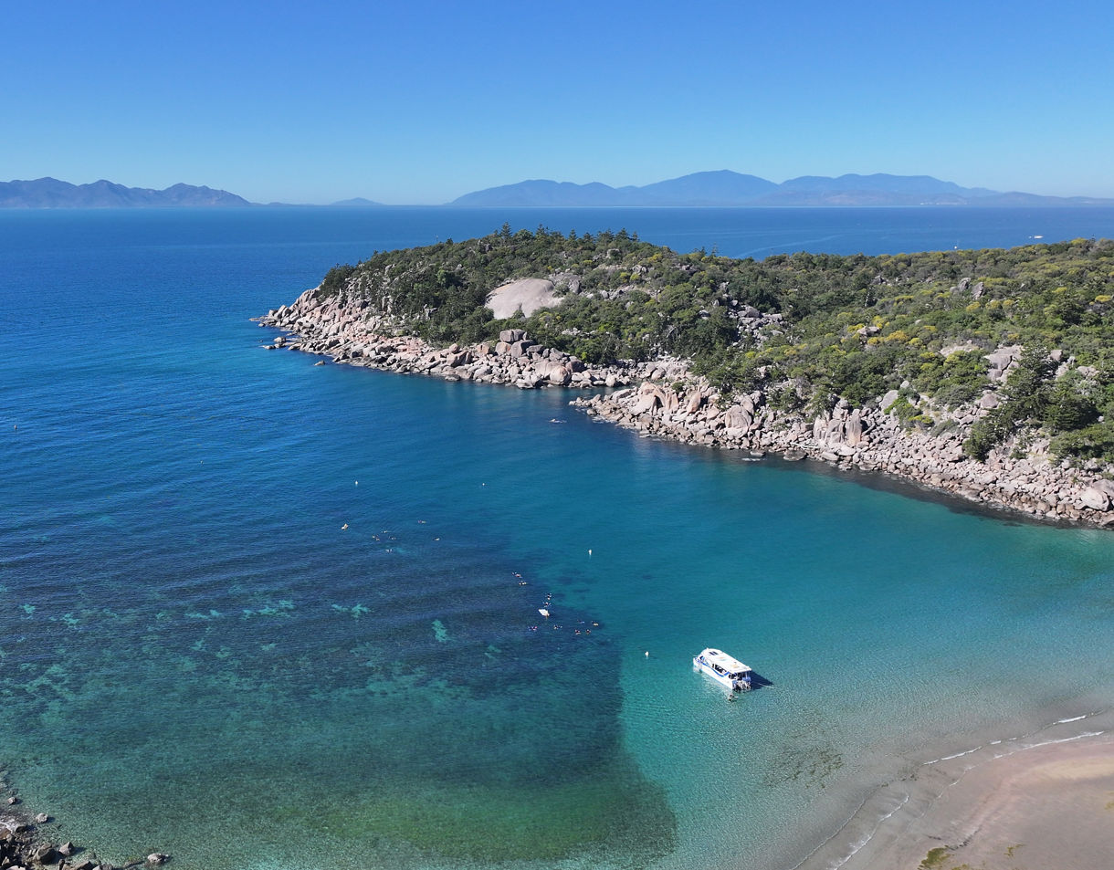 A sheltered bay with clear turquoise water, rocky shorelines covered in green vegetation and a small boat anchored near the beach