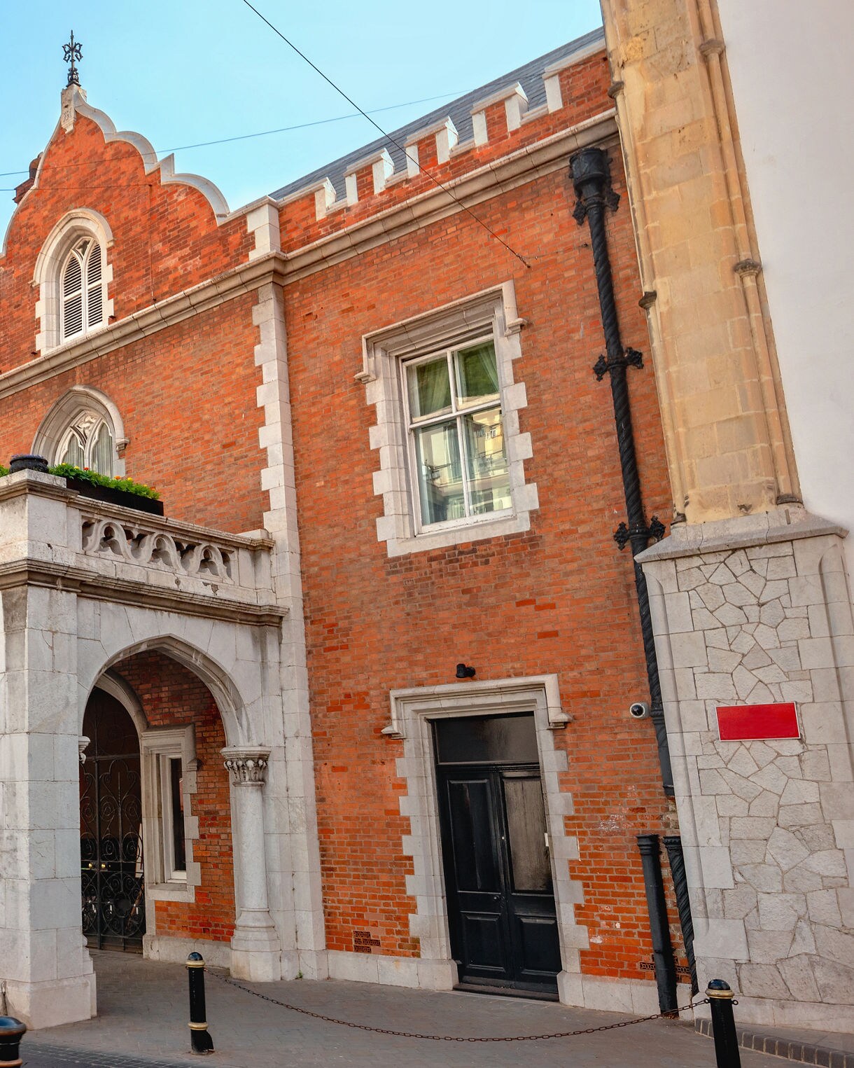 A historic red-brick building with a decorative white stone arched entrance, tall narrow windows and a flag flying overhead, set along a pedestrian street.
