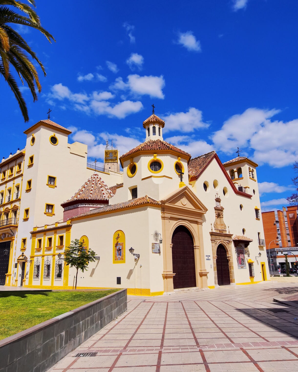 White and yellow Church of San Juan Bosco in Málaga, Spain, with tiled roofs, round windows and a clear blue sky above.