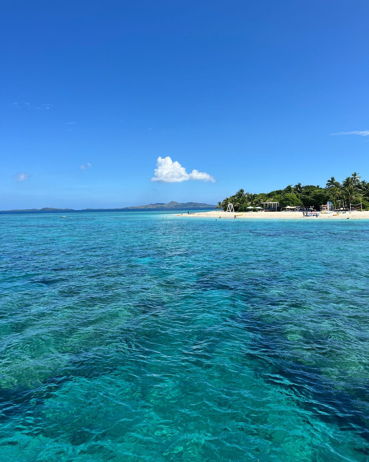 View of Malamala Island in Fiji with crystal-clear turquoise water, a white sandy beach and lush palm trees under a bright blue sky.