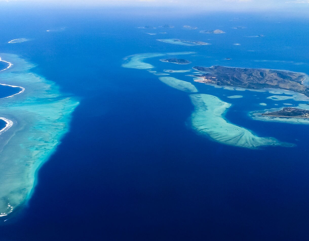 Aerial view of Fiji’s Mamanuca Islands showing turquoise coral reefs and deep blue ocean surrounding small, lush islands.