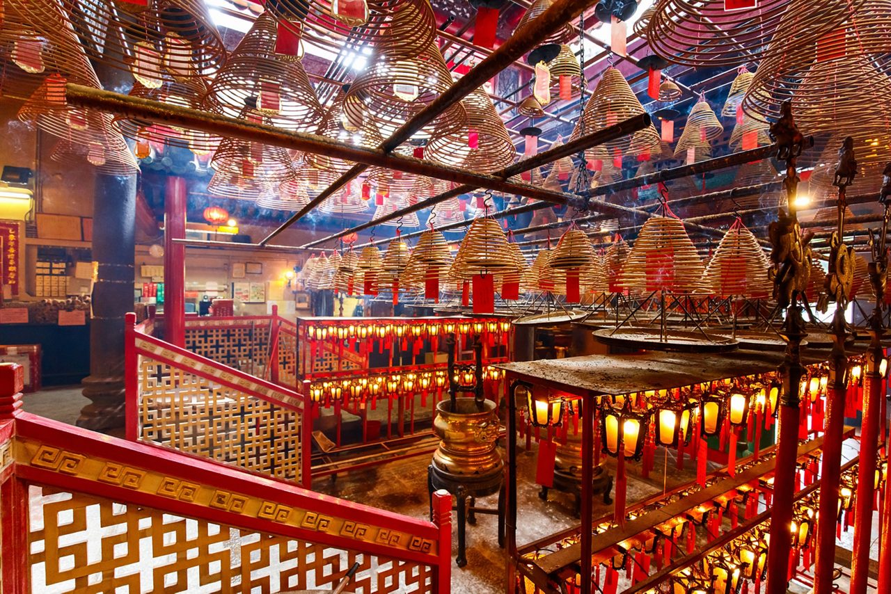  Interior of Man Mo Temple with spiral incense coils hanging from the ceiling and warm light illuminating red lanterns and railings.