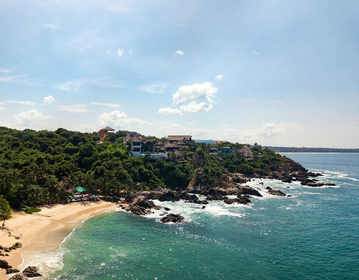 Secluded beach in Manzanillo with golden sand, rocky shoreline, lush green hills and houses overlooking the Pacific Ocean.