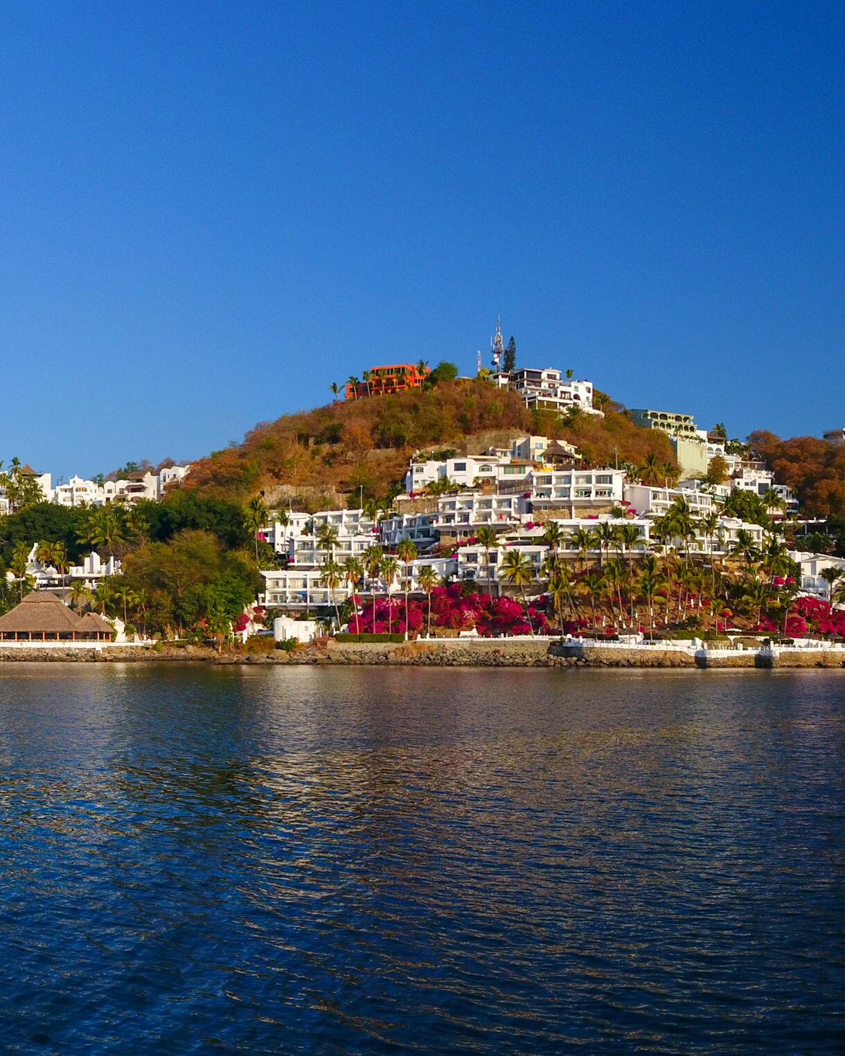 Panoramic view of Marina Villa del Mar in Manzanillo, featuring white hillside resorts, palm trees and yachts along calm blue waters.