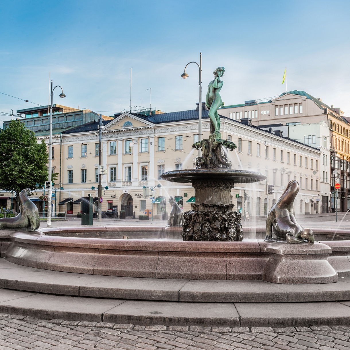 The Havis Amanda Fountain in Helsinki, featuring a bronze female statue surrounded by four sea lion sculptures with water jets, set in a city square.