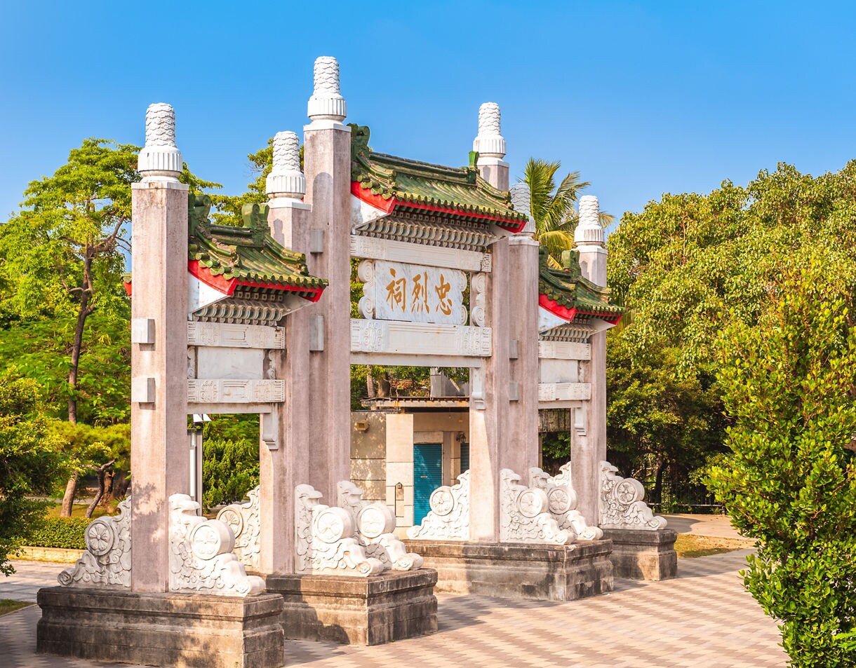 Ornate entrance arch of the Martyrs’ Shrine in Kaohsiung, Taiwan, featuring green-tiled roofs, stone carvings and surrounding trees under a bright blue sky.