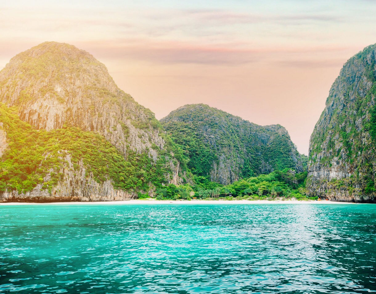 Maya Bay on the Phi Phi Islands with emerald water, white sand and steep limestone cliffs at sunset.
