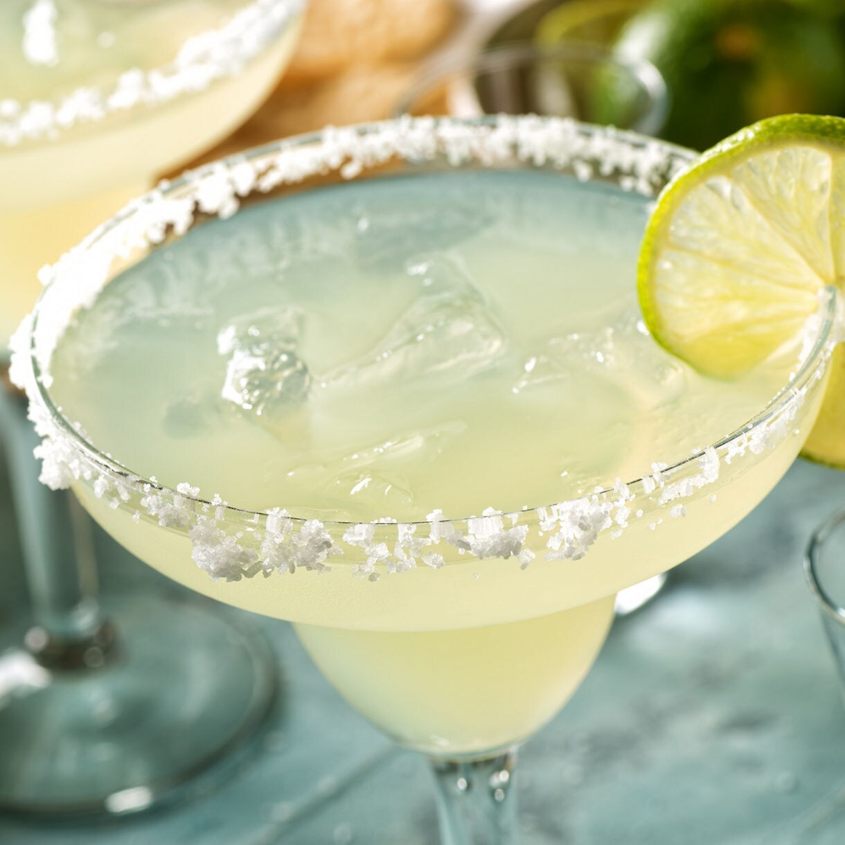 Close-up of a margarita glass rimmed with salt, filled with ice and garnished with a lime slice.