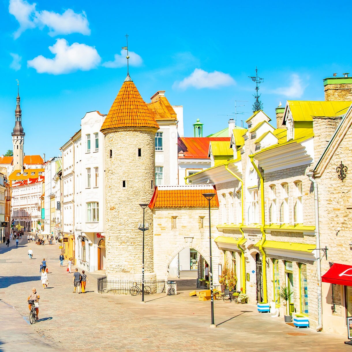 Viru Gate in Tallinn, Estonia, featuring two round medieval stone towers with red rooftops leading into the cobblestone streets of the Old Town on a sunny day.